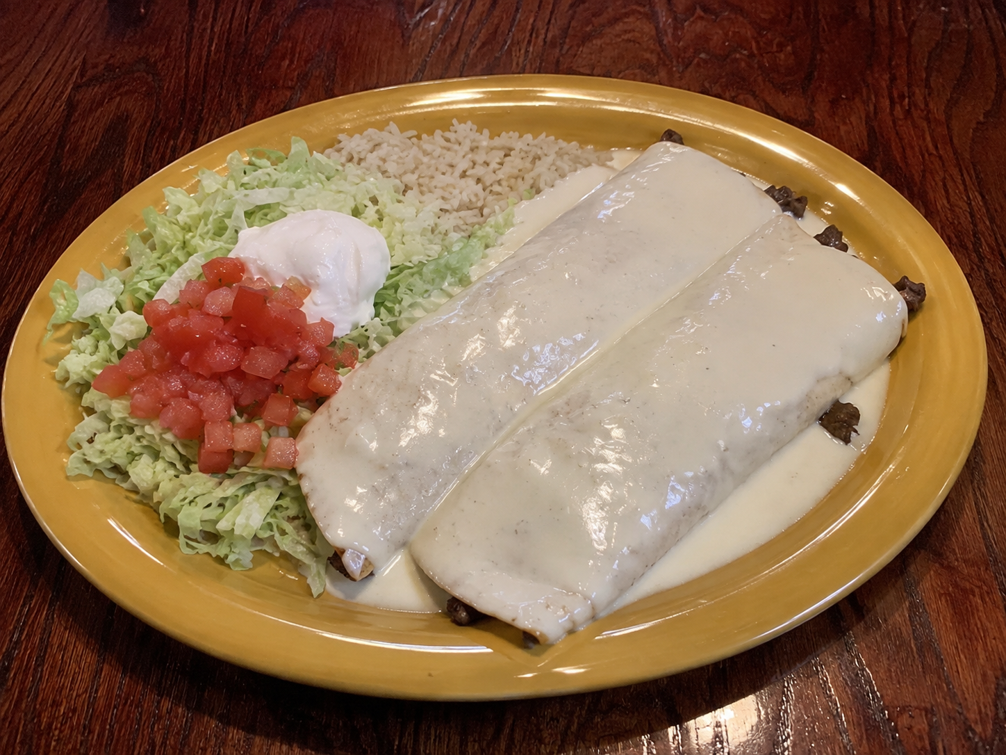 Steak burritos smothered in white cheese sauce with rice and pico de gallo